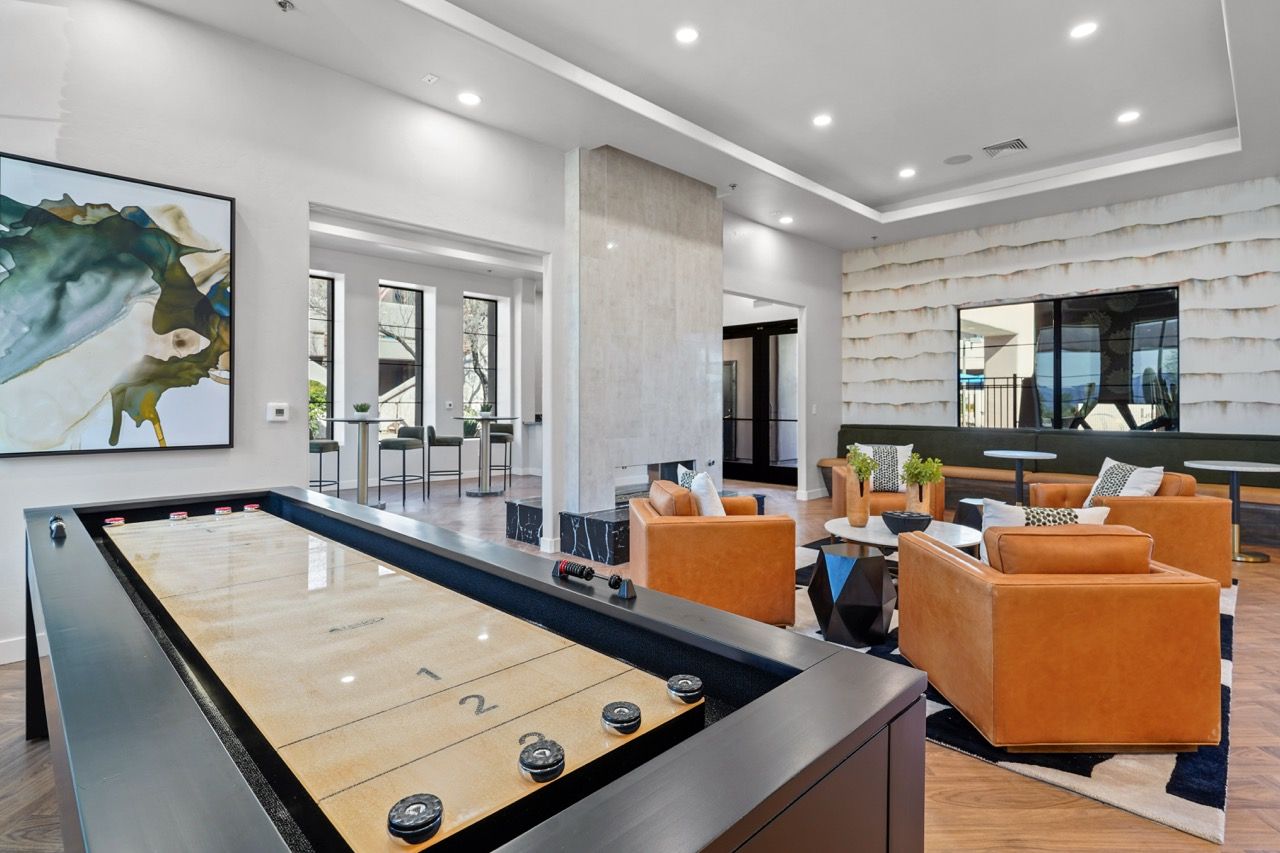 Modern communal lounge with a large pool table and tan leather seating under bright lights.