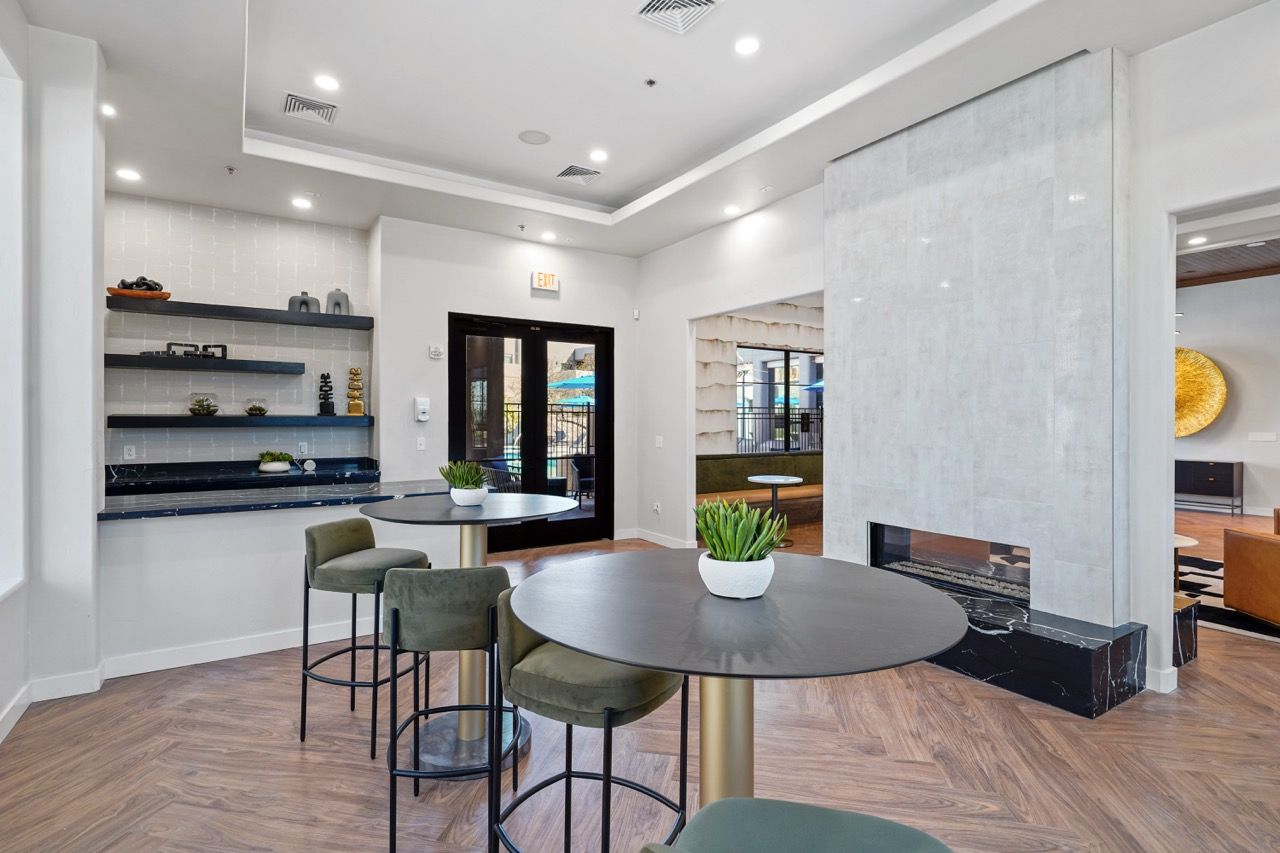Bright community lounge with round tables, green chairs, and wall shelving at Legacy Apartments at Dove Mountain in Marana, AZ.