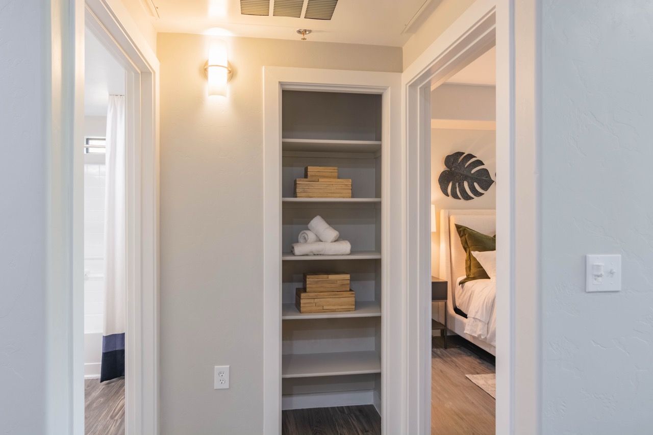 Hallway view of a built-in linen closet with open shelves, towels and wooden boxes, beside a bedroom at Legacy Apartments at Dove Mountain in Marana, AZ.