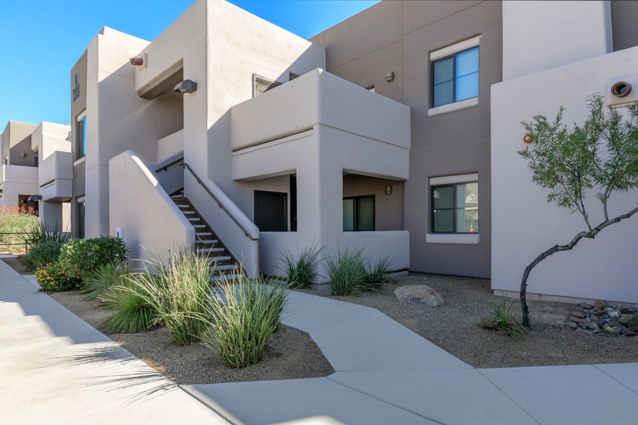 Exterior view of a modern multi-unit apartment complex with stairs and desert landscaping at Legacy Apartments at Dove Mountain in Marana, AZ.