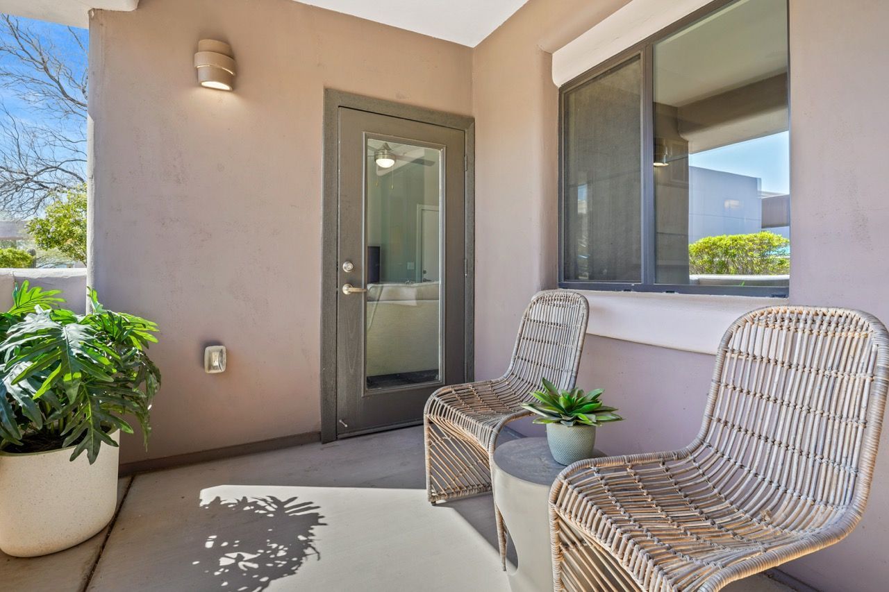 Balcony with two wicker chairs, a small plant, a door, and a large window at Legacy Apartments at Dove Mountain in Marana, AZ.