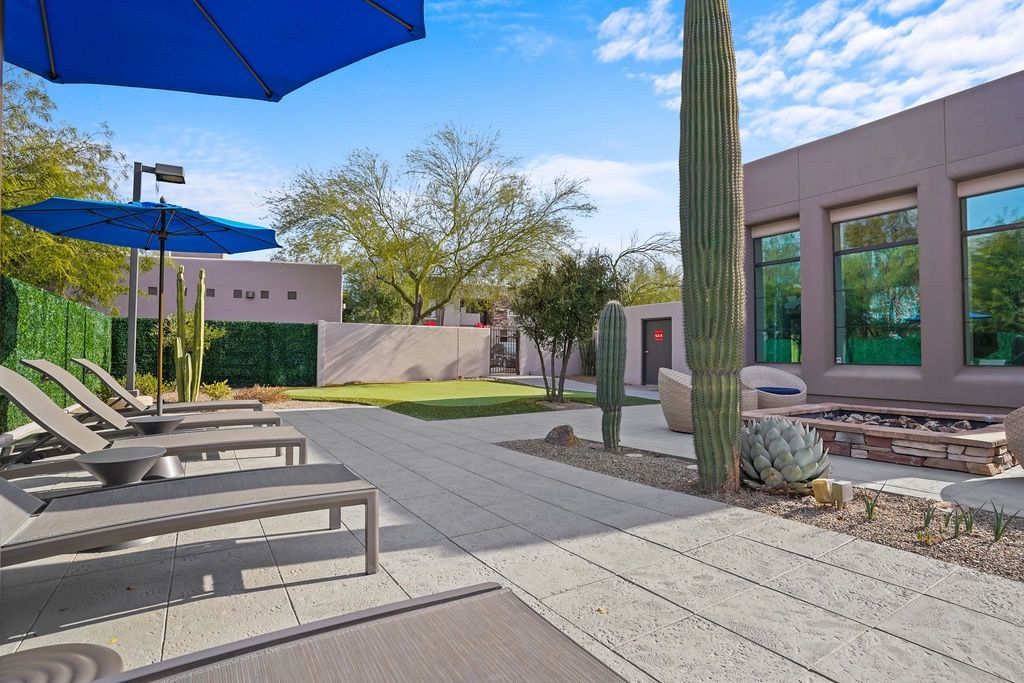 Outdoor communal lounge area with sun loungers, blue umbrellas, and desert landscaping at Legacy Apartments at Dove Mountain in Marana, AZ.