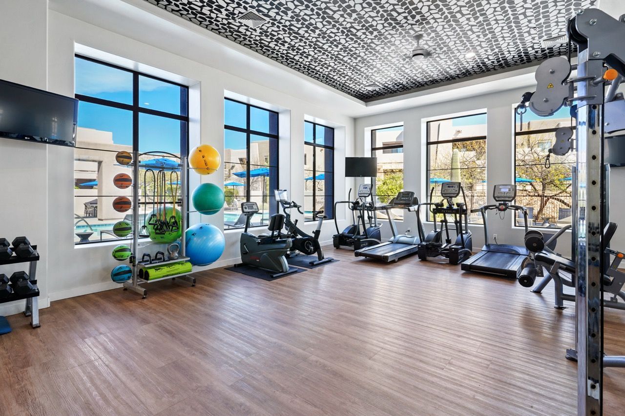 Bright on-site fitness center with treadmills, weights, and colorful exercise balls by large windows.