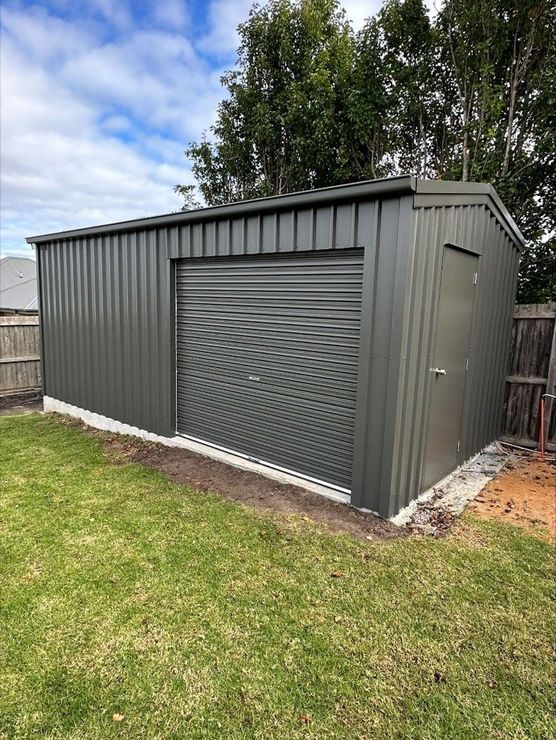 Exterior view of a secure, dark corrugated metal storage shed with a large roller door, representing reliable Storage Warrnambool and professional Storage Services Warrnambool.