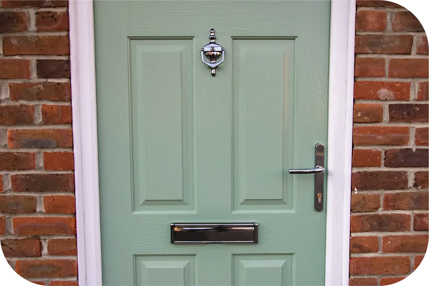 Sage green four-panel front door with a chrome knocker, mailbox, and handle, set into a red brick wall.