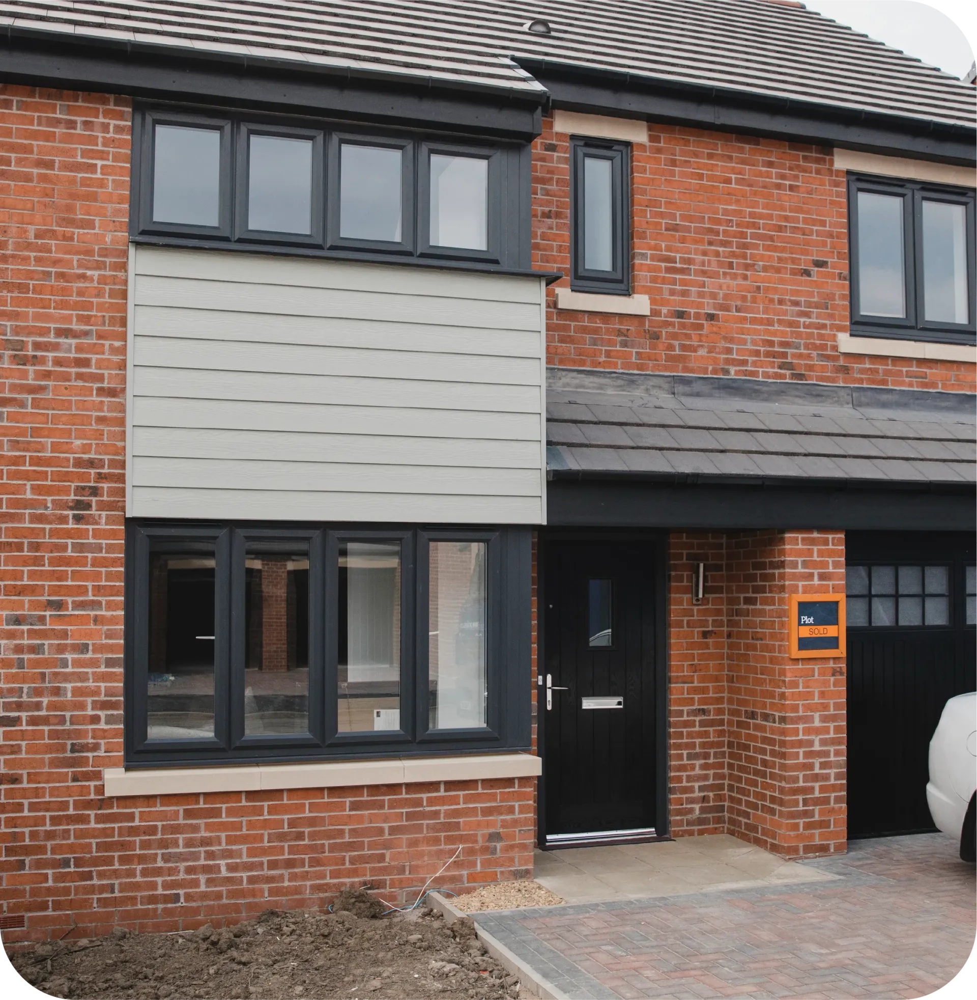 A two-story red brick house with dark window frames, a black front door, a garage, and a light-colored wood panel facade.