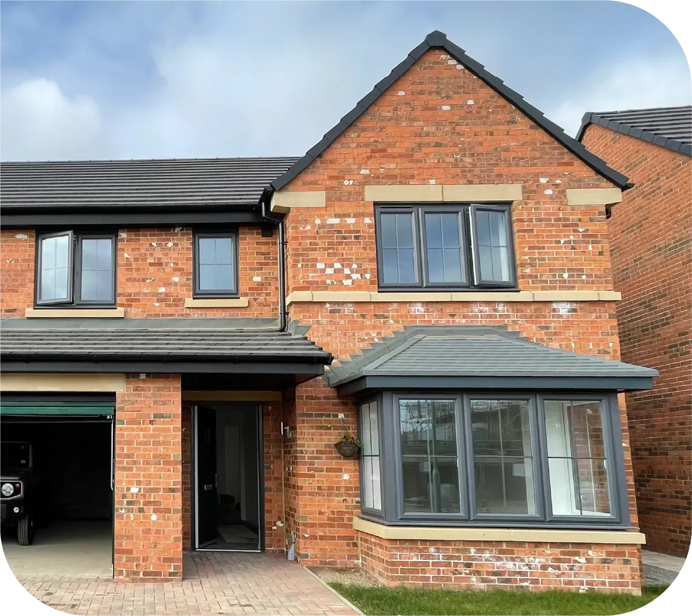 A two-story brick house with a dark roof, a front-facing garage, and a large bay window on the ground floor.