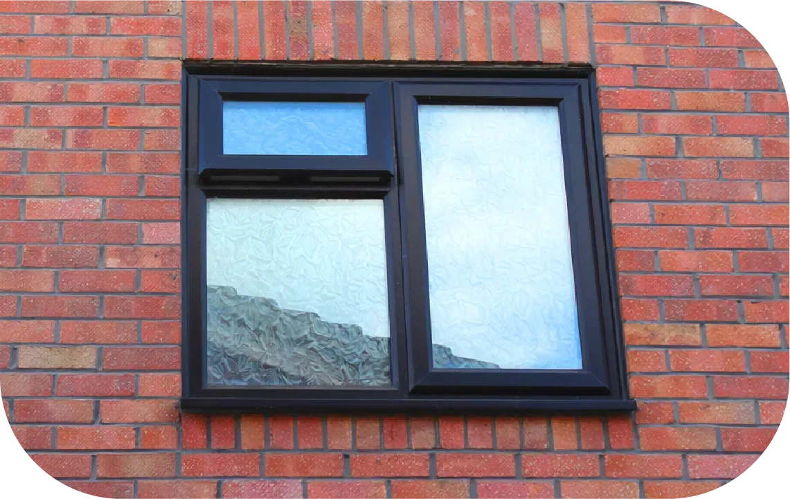 A black-framed, two-pane window with a small top-opening vent, set into a red brick wall.