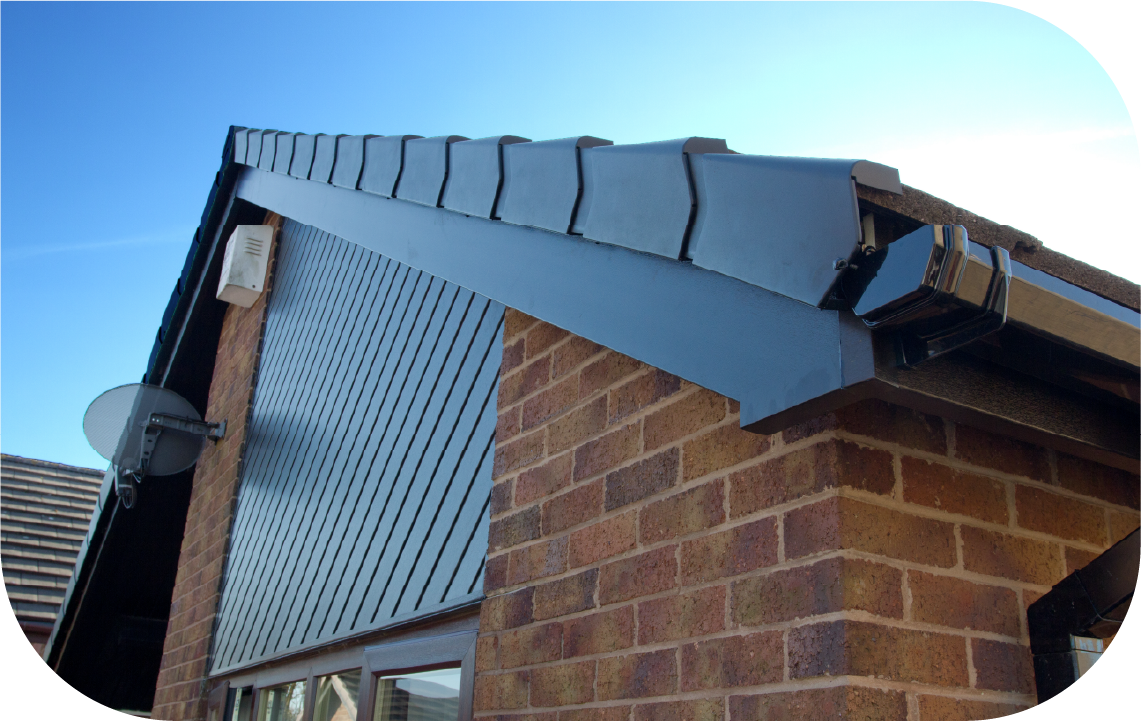 Close-up of a brick house corner featuring dark roof tiles, a black fascia board, and a patterned louvered wall panel.