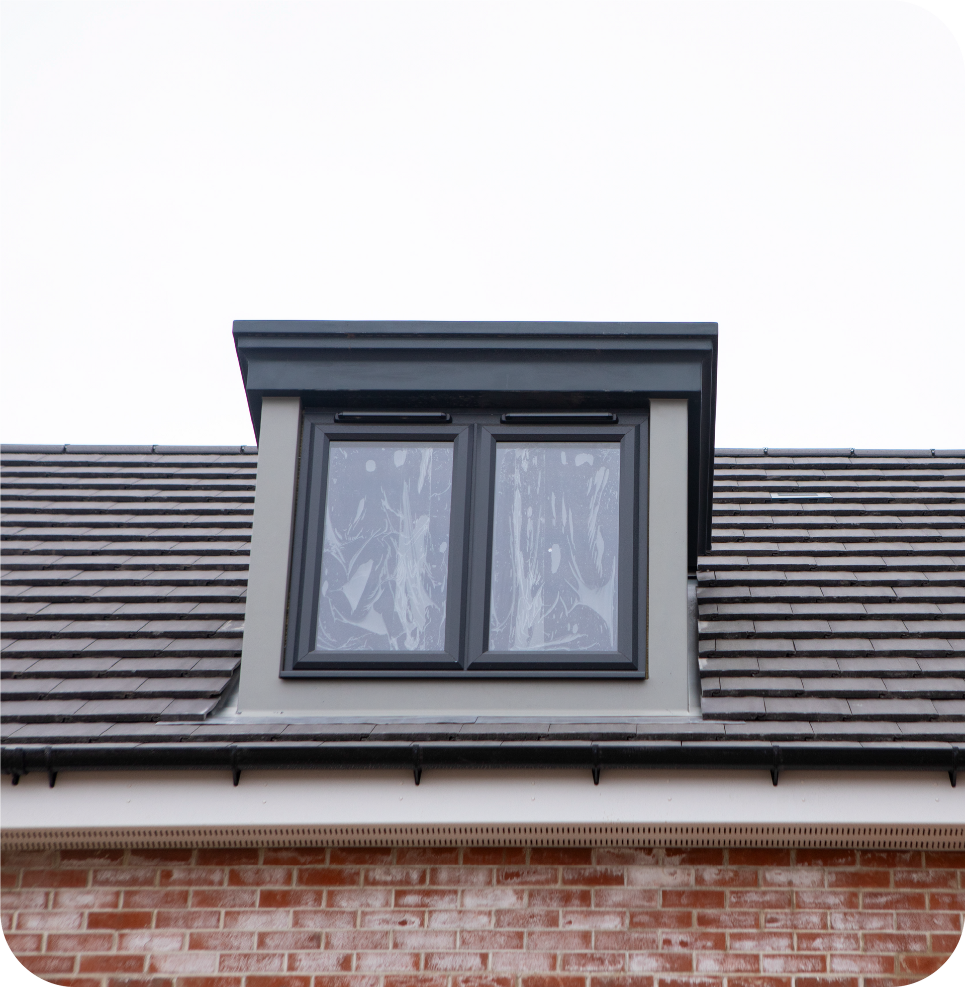 A black-framed dormer window sits on a tiled roof above a red brick wall.