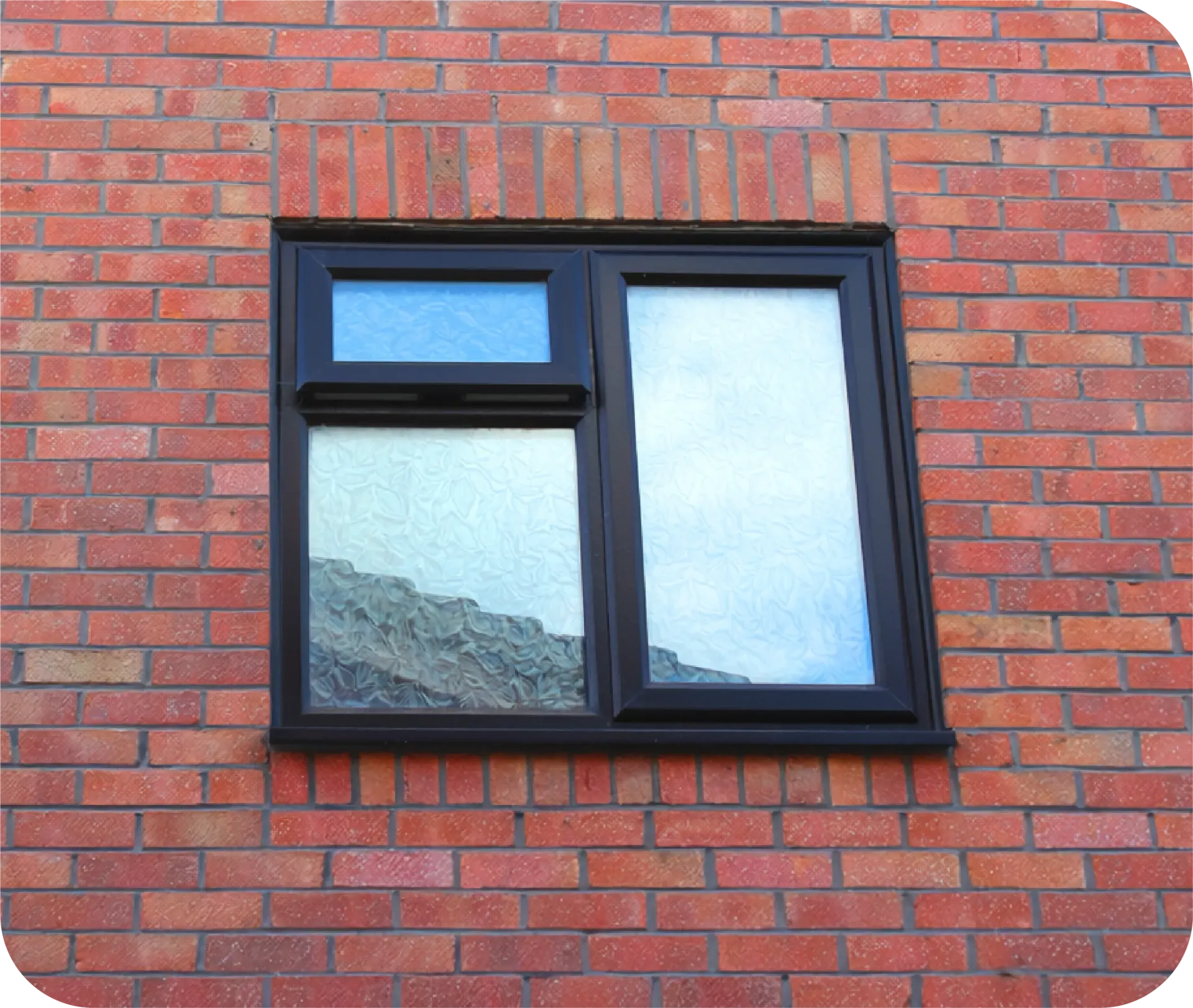 A rectangular, dark-framed window with two panes set into a red brick wall, with the smaller top pane open.