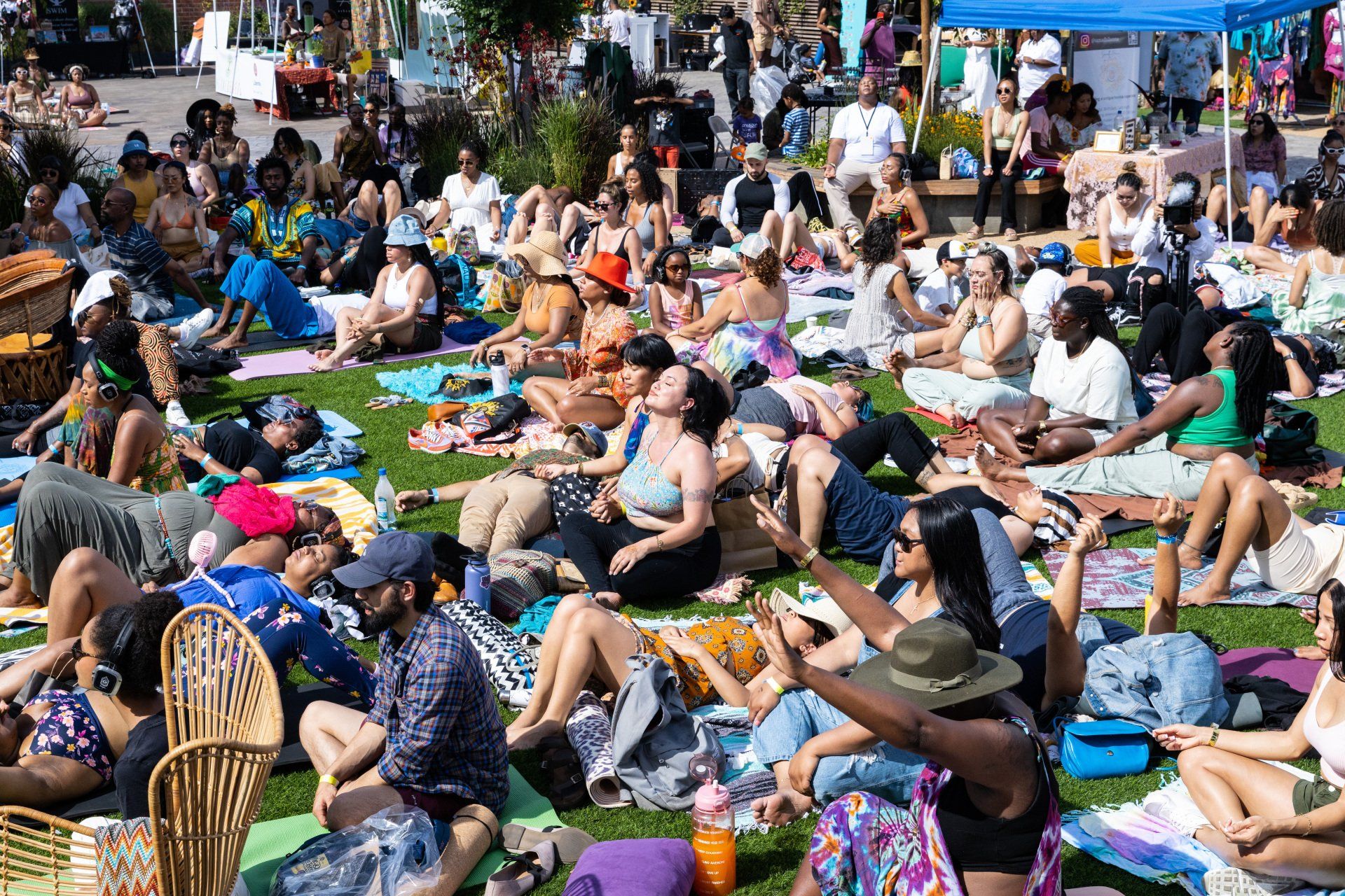A large group of people are sitting on the grass at Sol & Sound wellness festival.