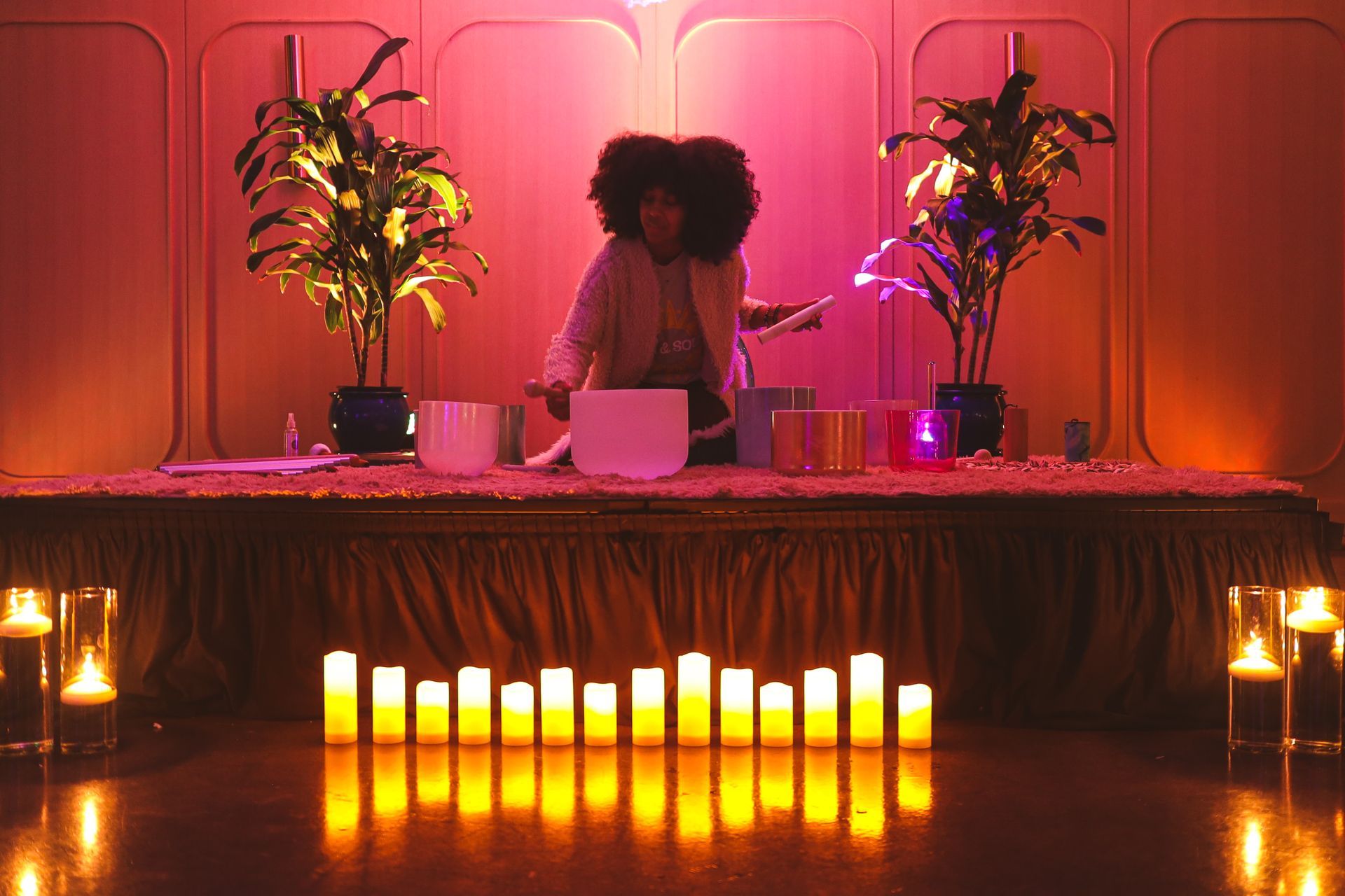 A woman is sitting on a stage with sound bowls and candles.
