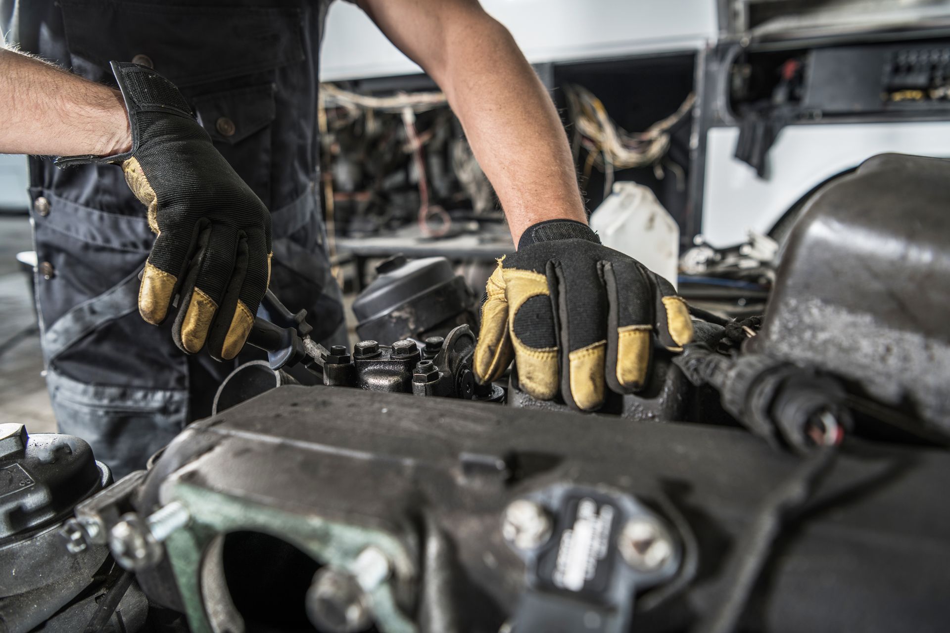 Mechanic wearing black-and-yellow gloves working on an engine in a garage.