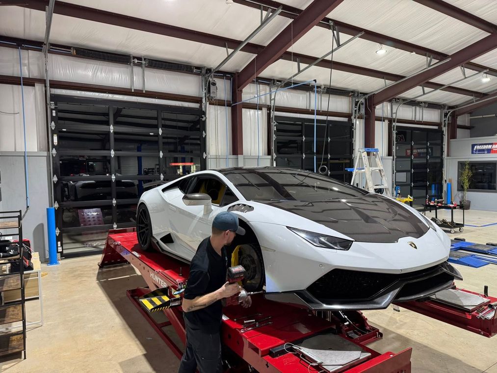 Mechanic inspects a white sports car on a red lift in an auto garage.