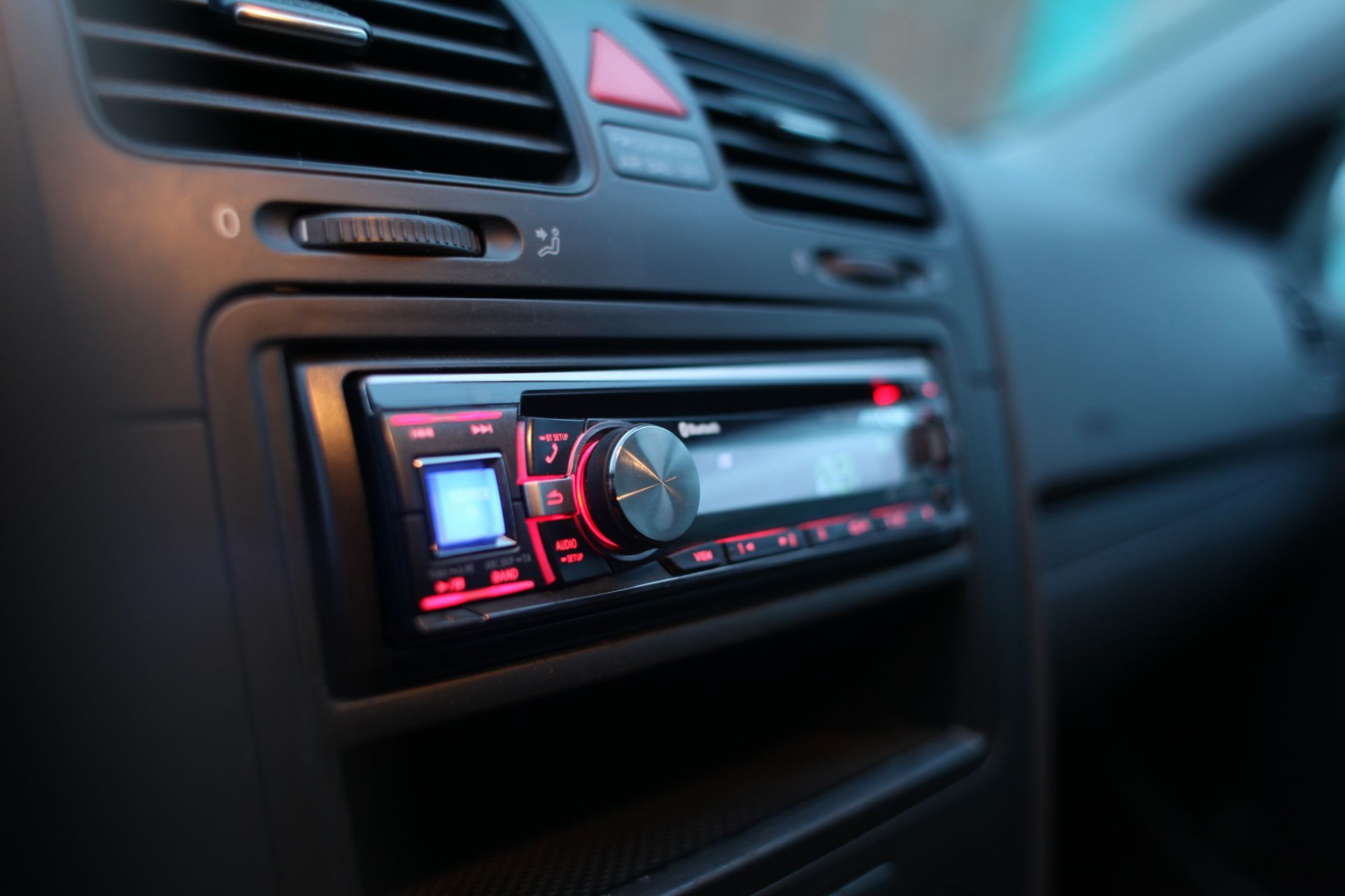 Car stereo with red-lit display and large volume knob in a car dashboard