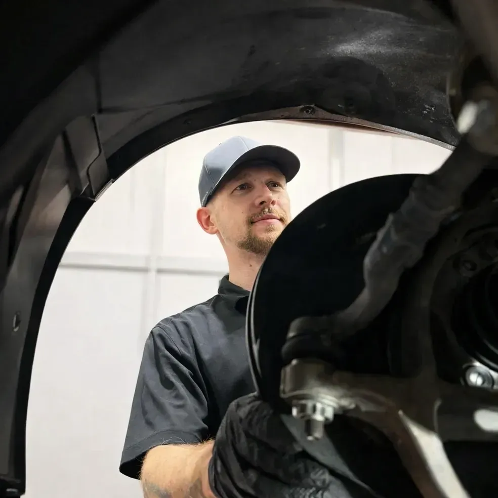 Mechanic in dark workwear inspecting a vehicle wheel well with a tire removed