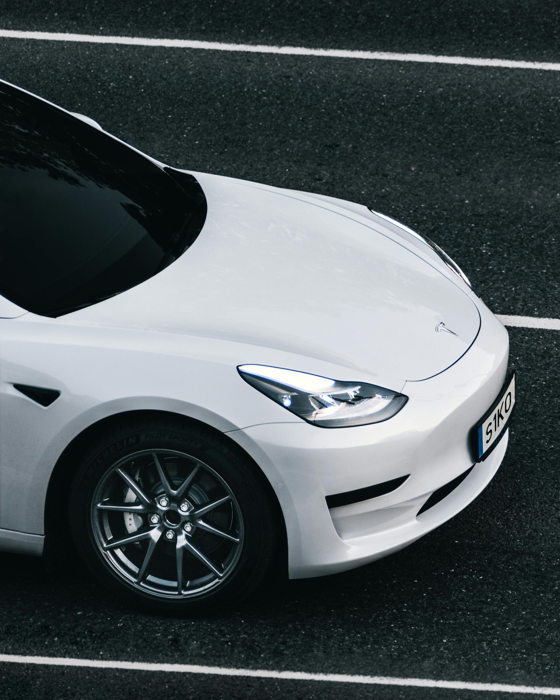 White sedan on a wet road, viewed from above at an angle.