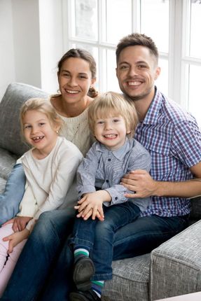 Family of four sitting on a gray couch, smiling in a bright living room.