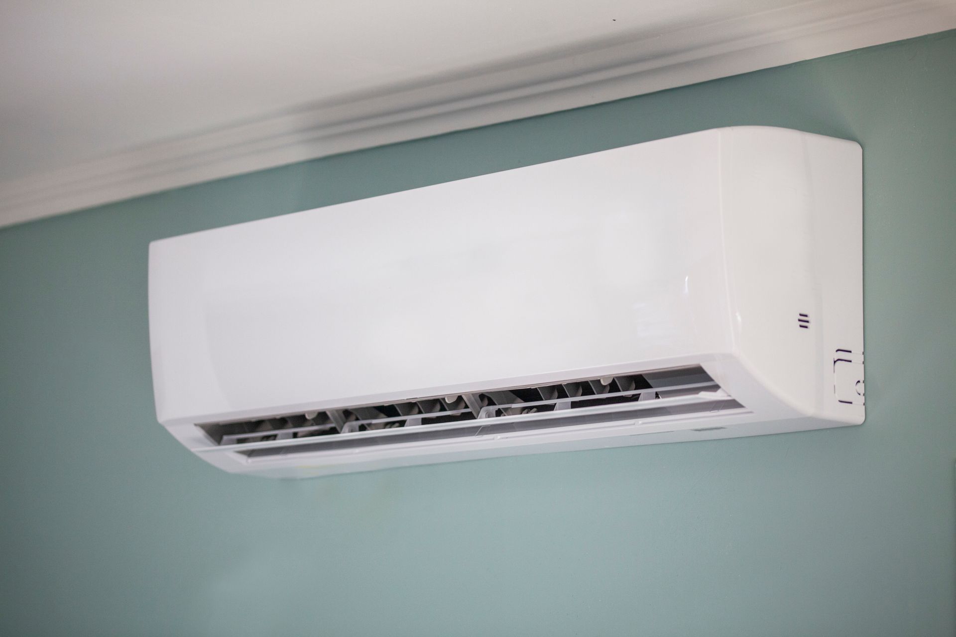 White wall-mounted air conditioning unit against a light teal wall, near a white ceiling trim.
