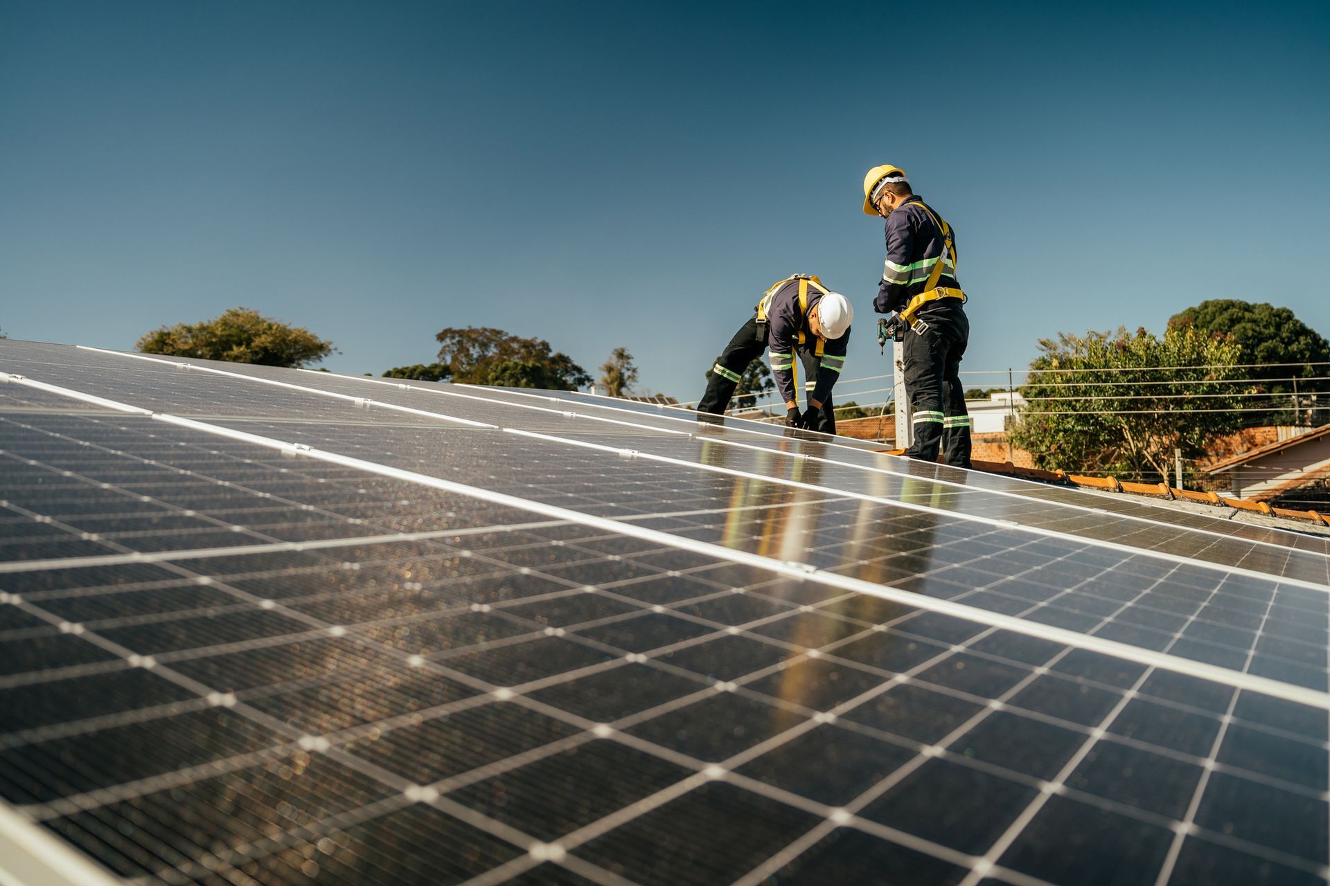 Two workers in safety gear installing solar panels on a rooftop under a blue sky.