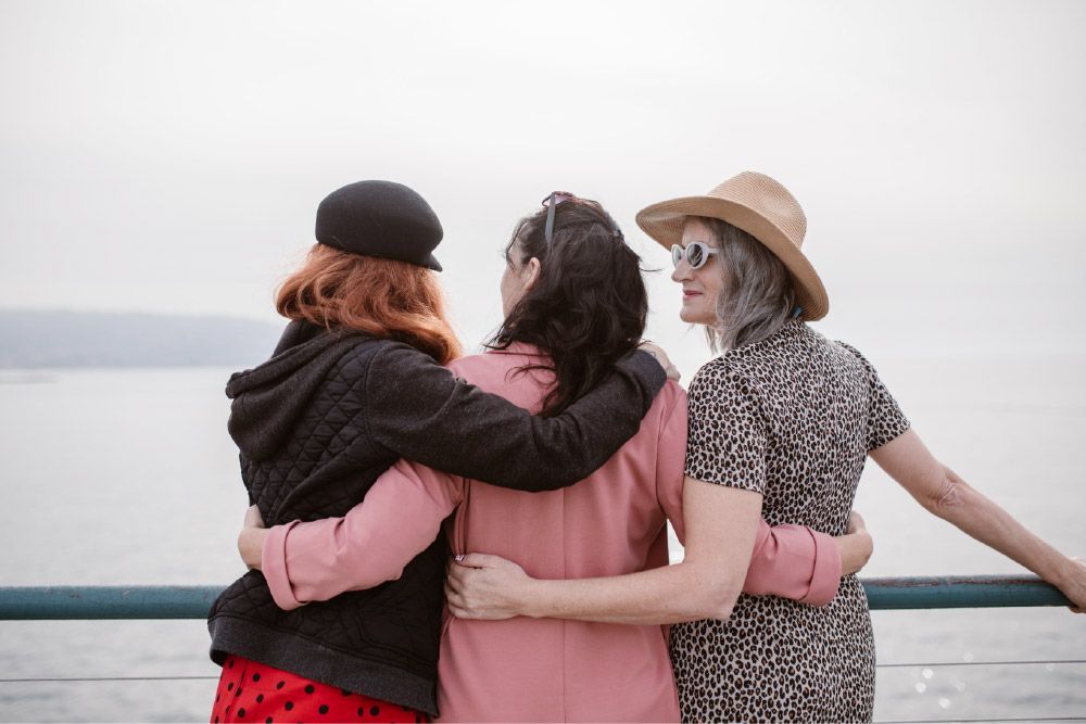 Three women with their arms around each other looking out over the water