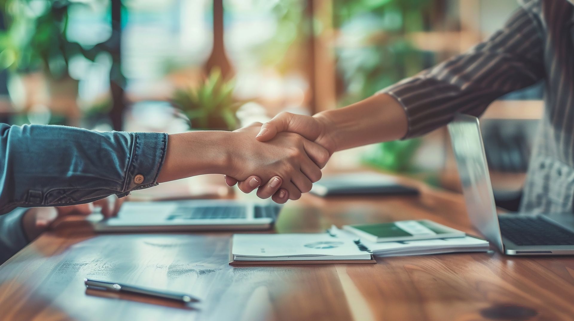 Two people are shaking hands over a wooden table.
