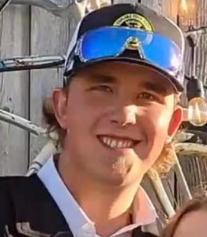 A young man wearing a baseball cap and sunglasses is smiling.