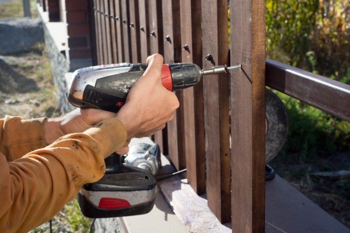 Person using a power drill to screw a wooden fence post into a railing.