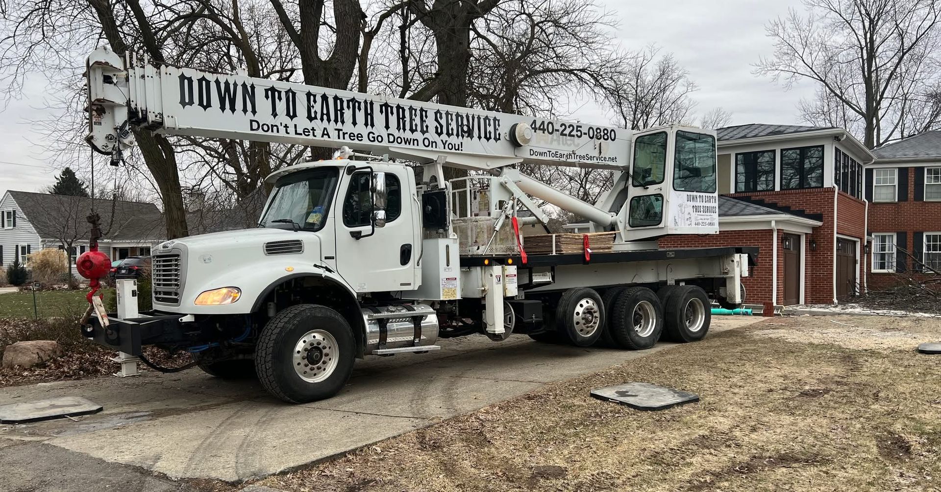 White crane truck parked on a gravel driveway next to a brick house; 