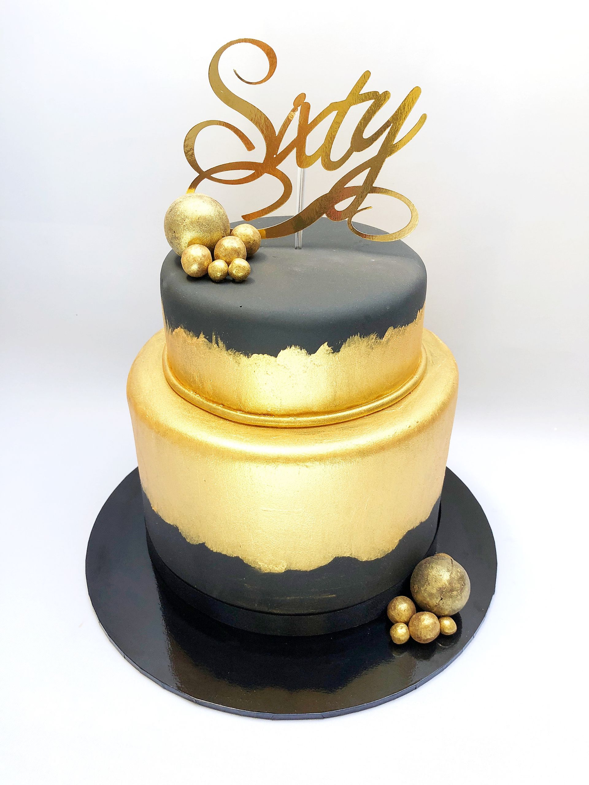 Two tier cake, covered in black fondant with gold detailing, gold balls, and gold 