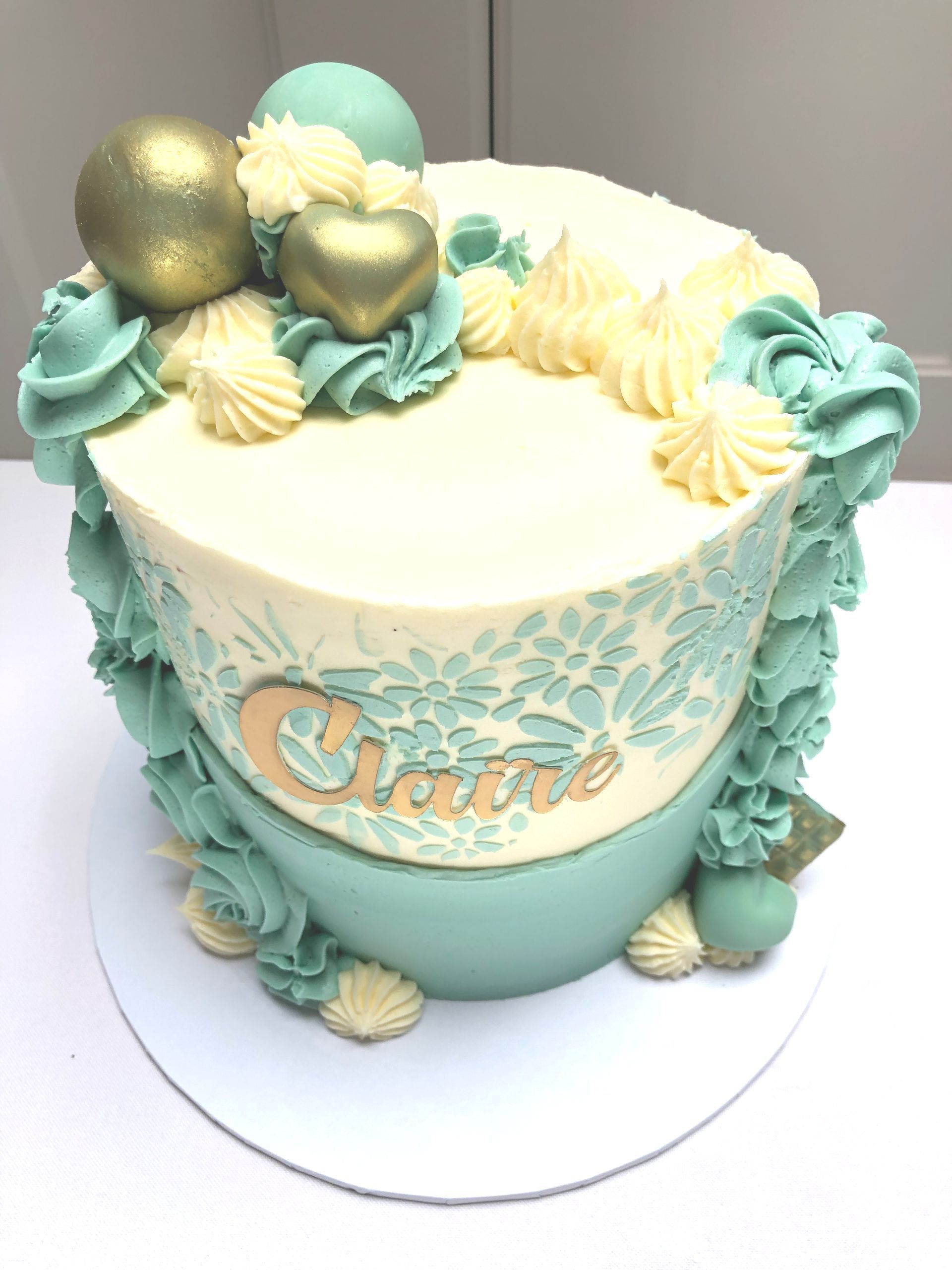 Ivory Buttercream covered cake with Tiffany blue buttercream stencil and piping work and a name in gold on the side of the cake.