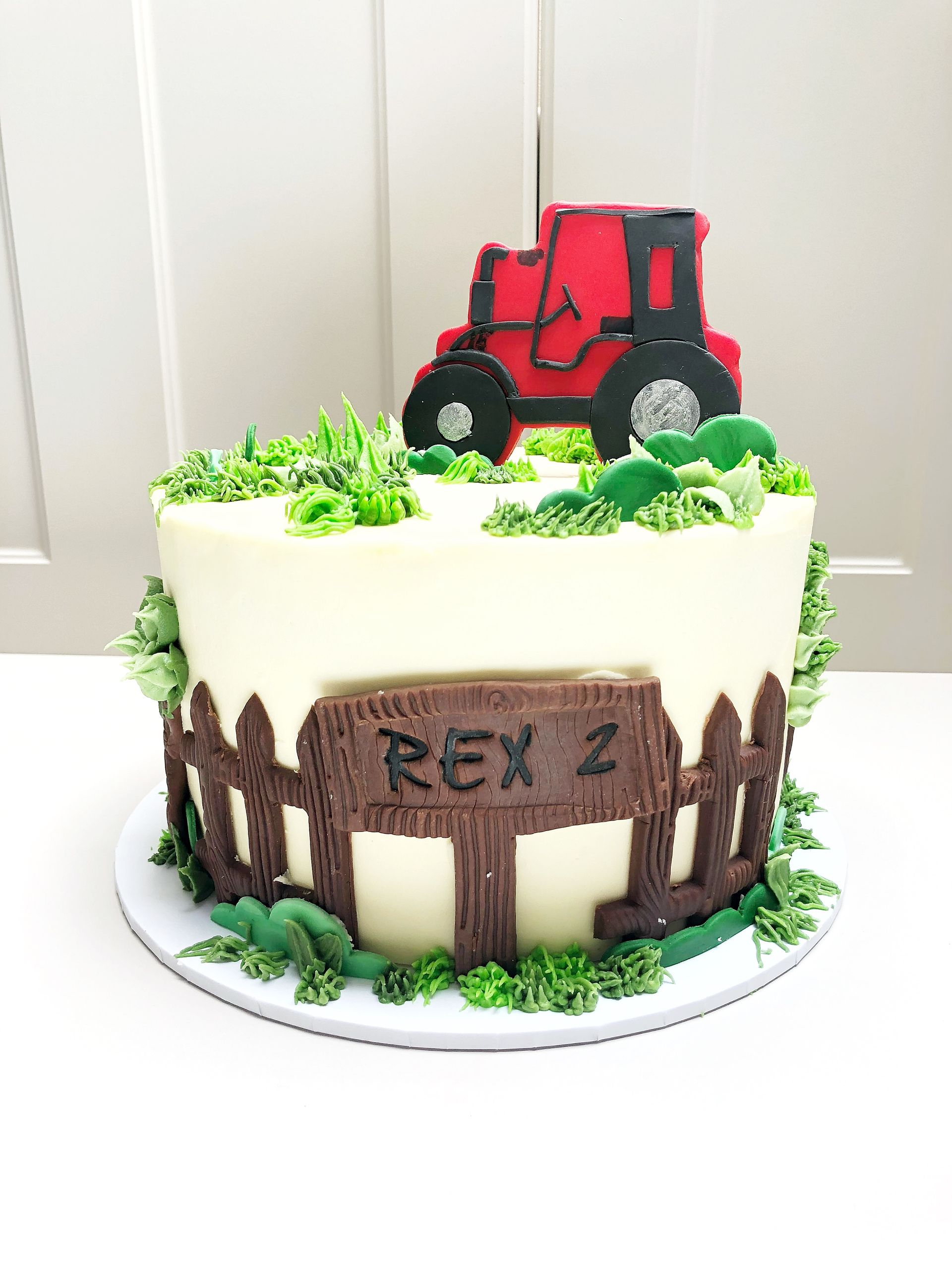 Tractor themed cake with fondant tractor, shrubs, grass and fencing details.