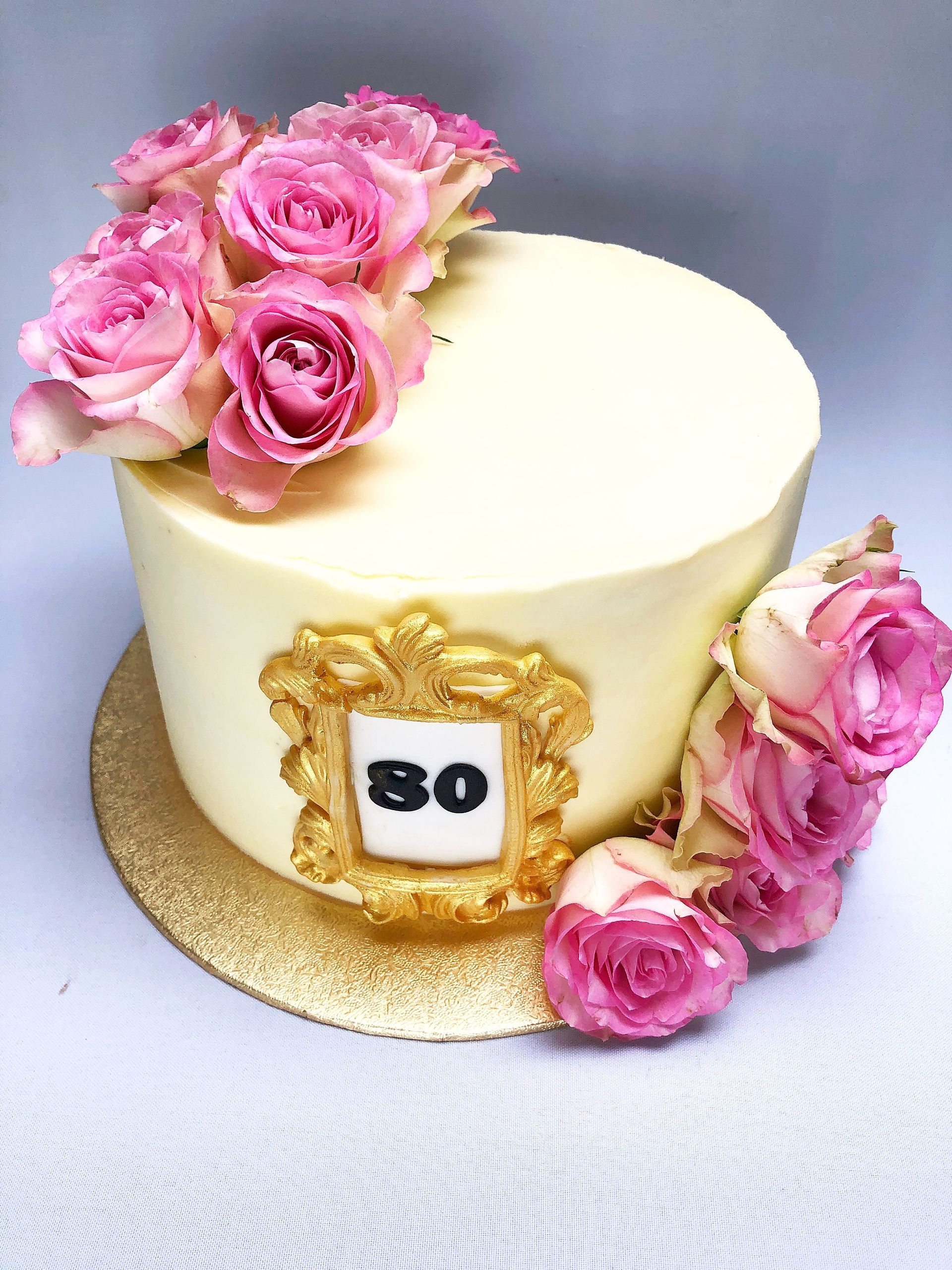 Ivory buttercream covered cake with gold fondant frame with the number 80 in the frame, and pink roses adorning the cake.