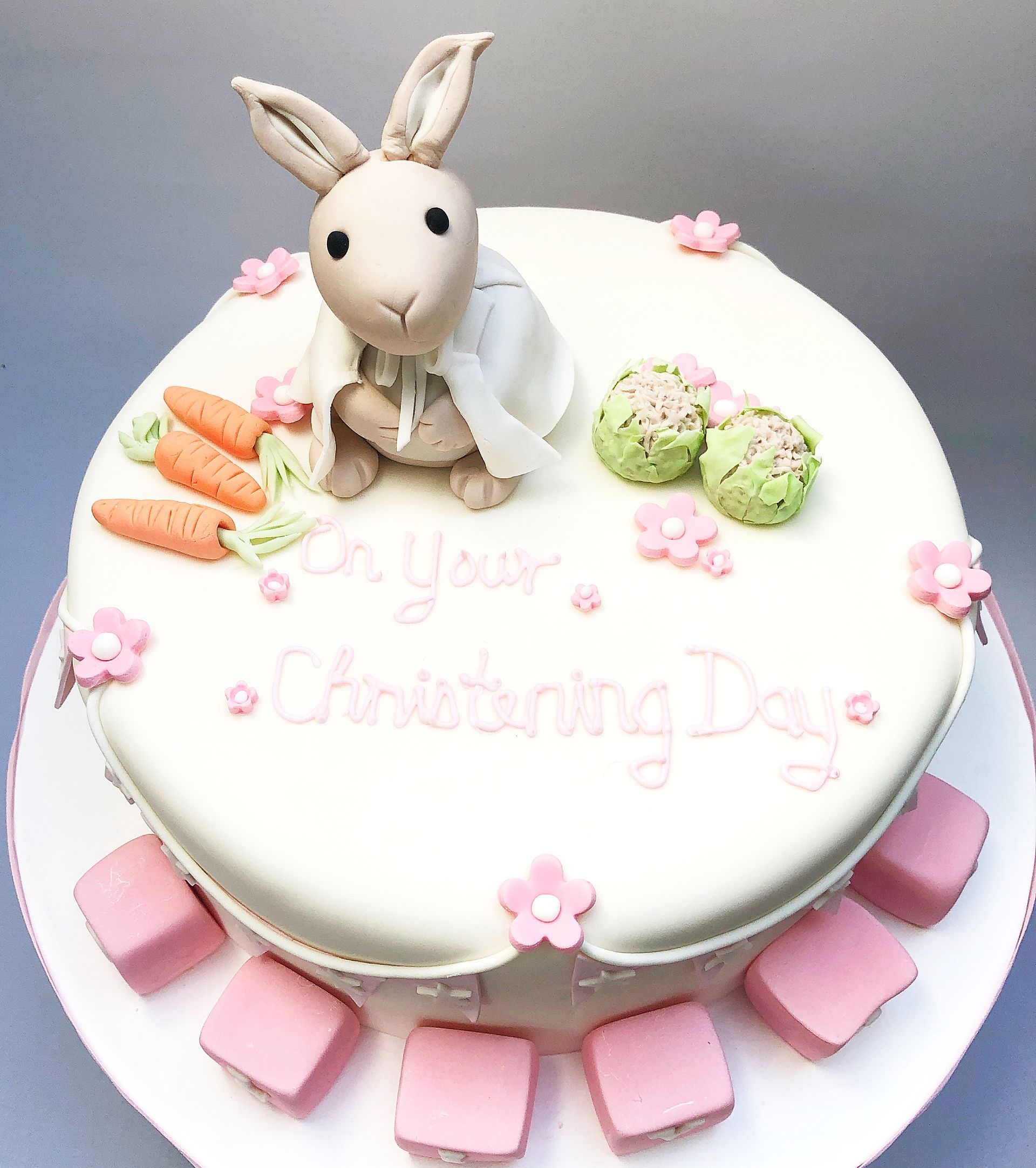 Fondant covered Christening cake with a  Peter Rabbit theme. A fondant rabbit, carrots, cauliflowers, and flowers are used to decorate the cake.
