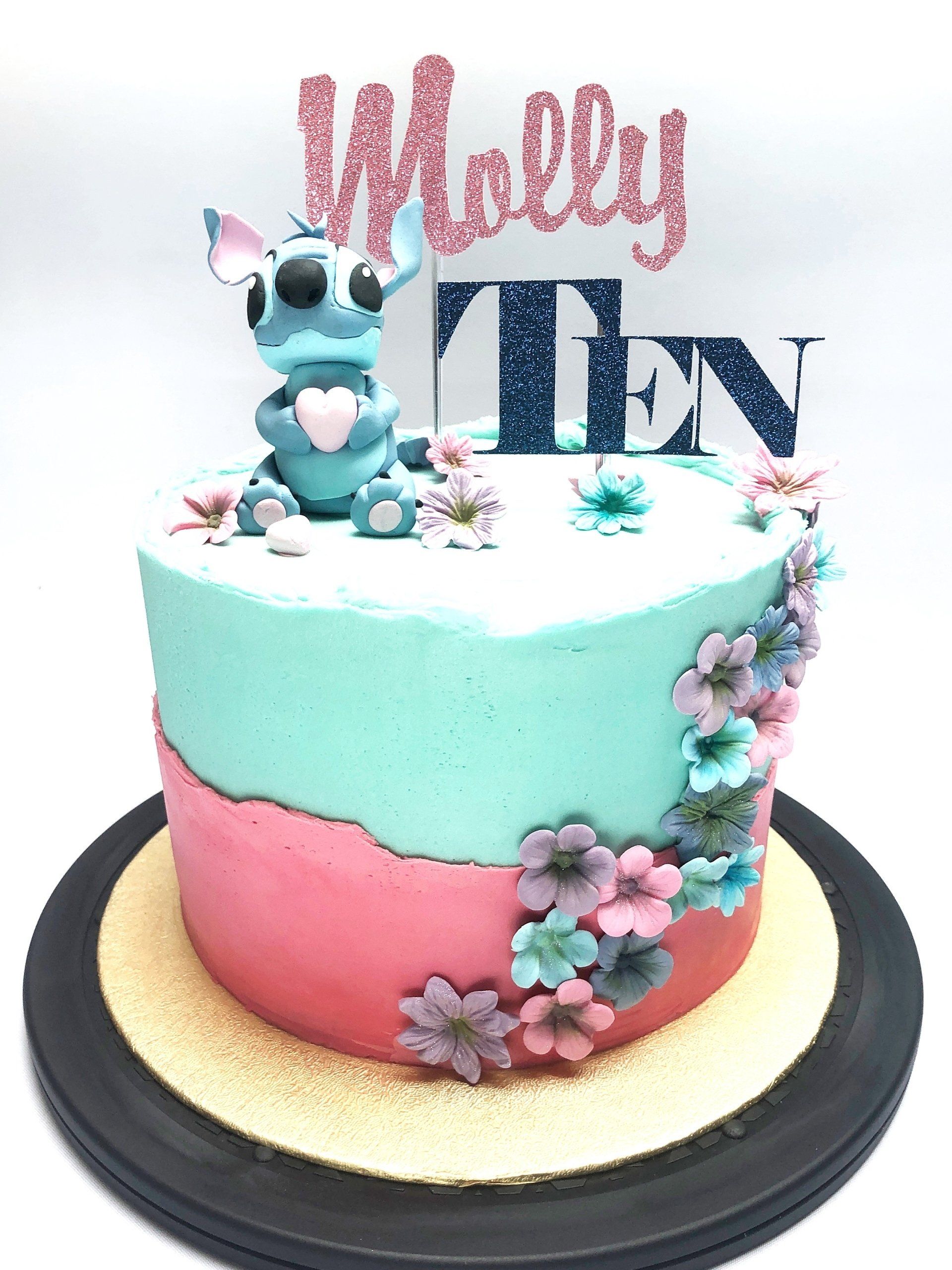 Adorable Stitch themed cake with fondant Stitch character, and fondant flowers. The cake has pink and blue buttercream icing and a topper in pink and blue saying 