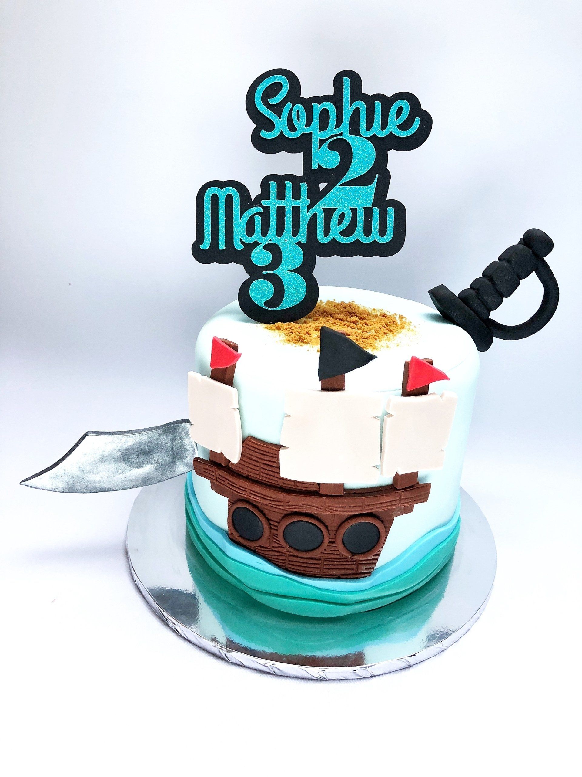 Pirate themed cake with fondant pirates sword, pirate ship and waves detail. Blue and black cake topper.
