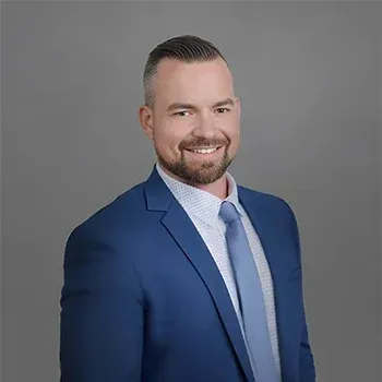 Man in a blue suit smiles at the camera, light skin, short brown hair and beard.