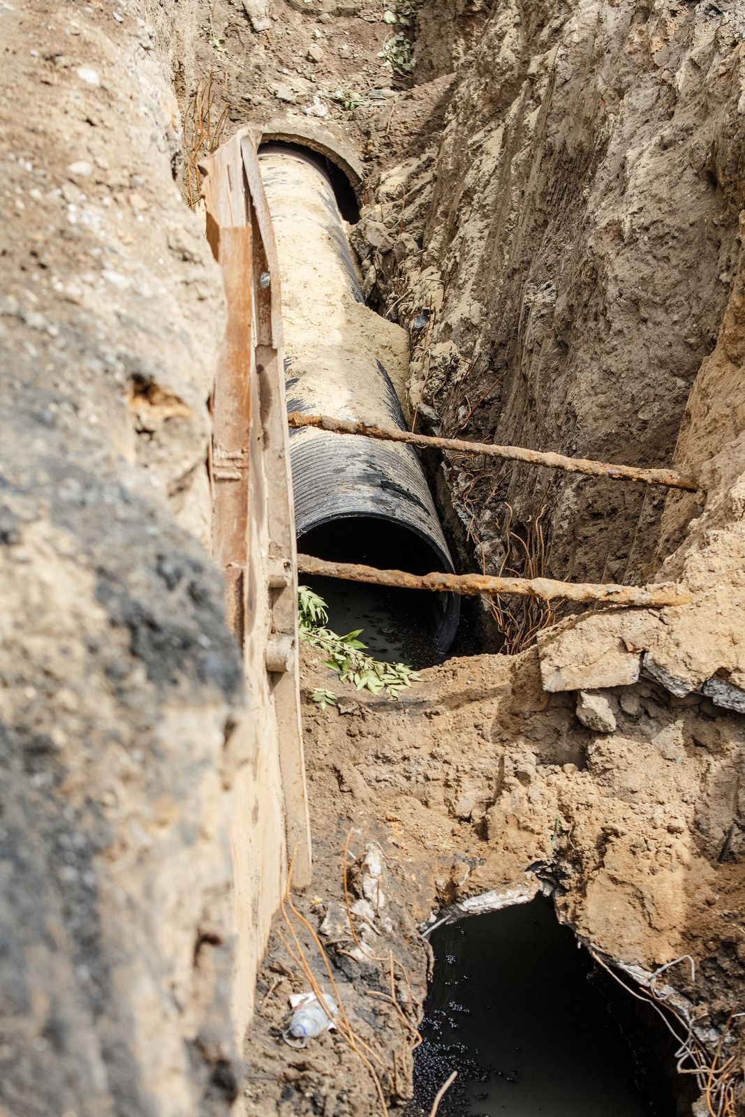 A black sewer pipe in a trench, with a wooden support structure, in a construction site.