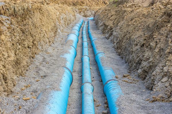 Blue pipes in a trench, ready for burial. Surrounded by gravel and dirt.