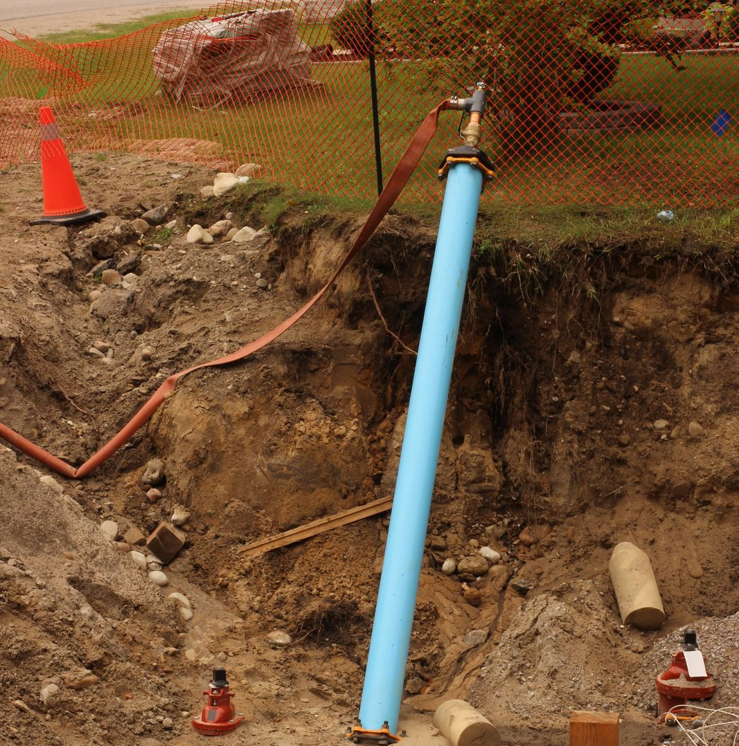 Construction site: blue pipe rising from a trench, orange safety cone, and dirt.