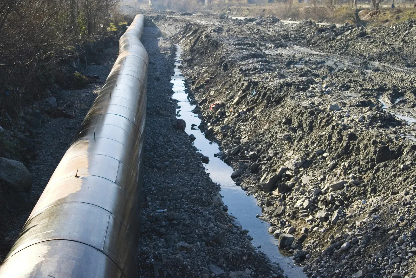 Large metal pipe laid in a trench alongside a narrow stream.
