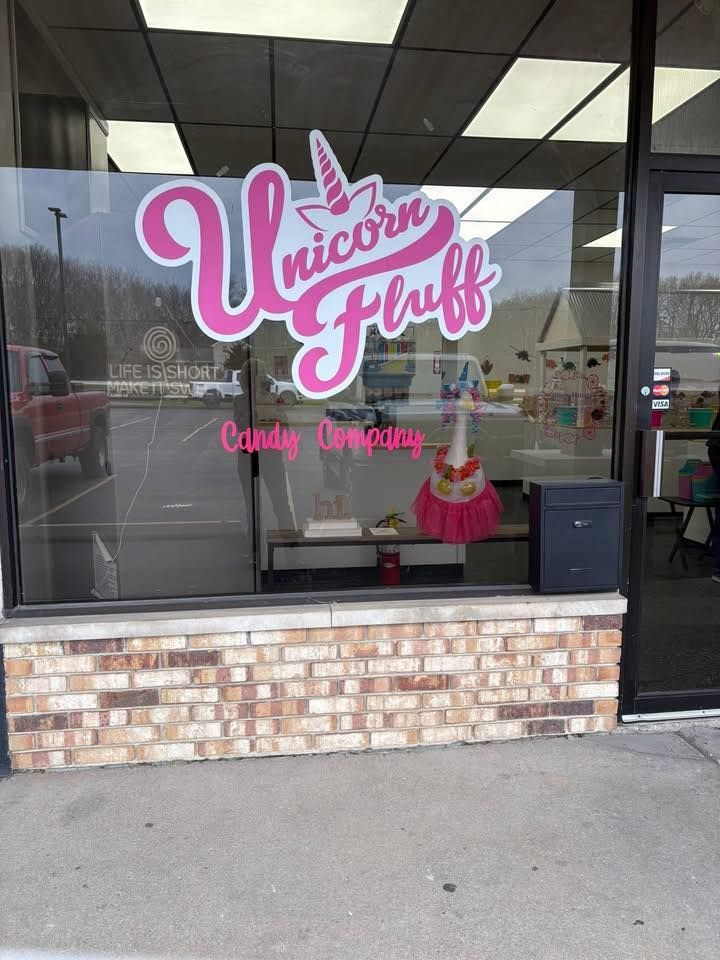 Storefront window for Unicorn Fluff Candy Company with a pink logo and a whimsical unicorn decoration inside.