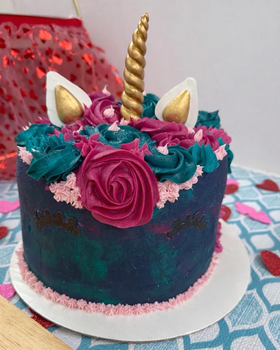 Unicorn-themed cake with dark blue and green marbled frosting, a gold horn, ears, and magenta floral frosting rosettes.