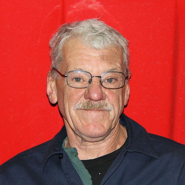 A man with glasses and a mustache is standing in front of a red curtain