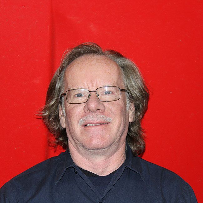 A man wearing glasses is smiling in front of a red background