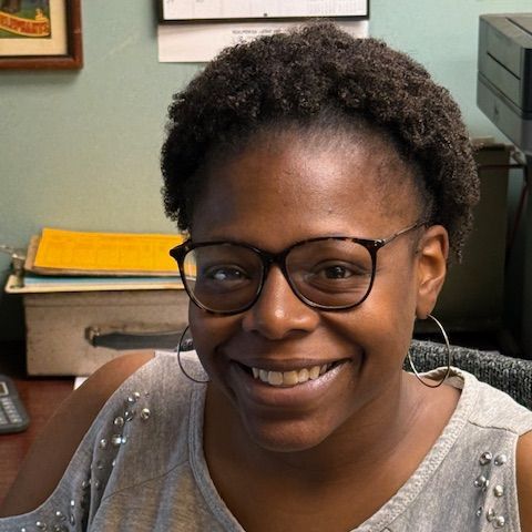 A woman wearing glasses and hoop earrings is smiling for the camera.