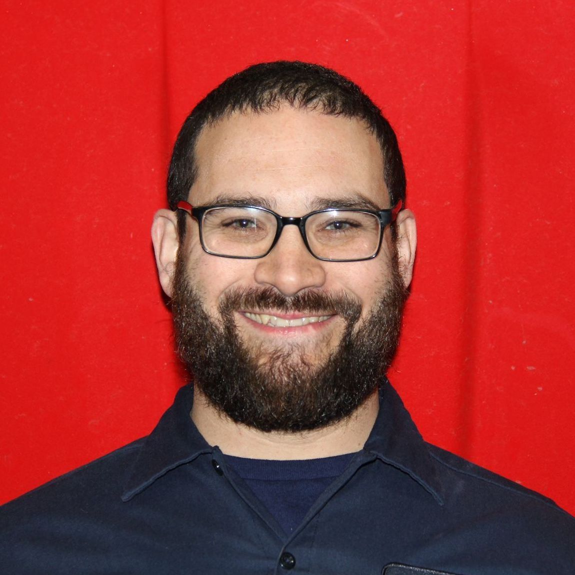 A man with a beard wearing glasses and a blue shirt