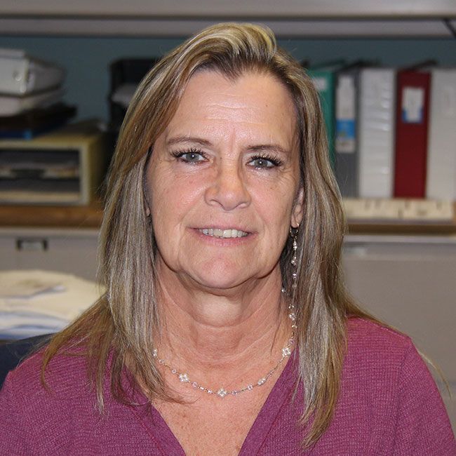 A woman wearing a purple shirt and a necklace is smiling for the camera.