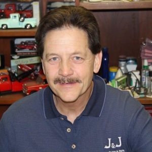 A man with a mustache wearing a blue shirt that says j & j